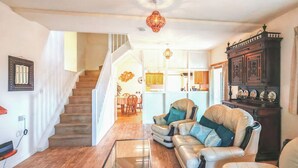 Un vaste salon doté d’un parquet, d’une table basse en verre, de deux canapés en cuir avec des coussins, d’un buffet en bois foncé et d’un escalier menant à un espace cuisine.