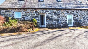 Un bâtiment en pierre avec un toit en pente, deux fenêtres et une porte.
