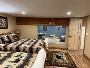 Een slaapkamer met een groot bed, een houten hoofdbord, een vloerkleed met een ontwerp van een beer, en een deur die naar een andere kamer leidt.