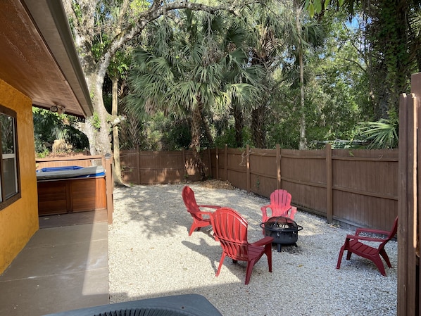 A backyard with a wooden deck, a hot tub, and red Adirondack chairs.