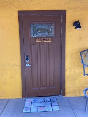 A brown door with a 'Key West' sign above it, a peephole, and a small window with glass blocks.