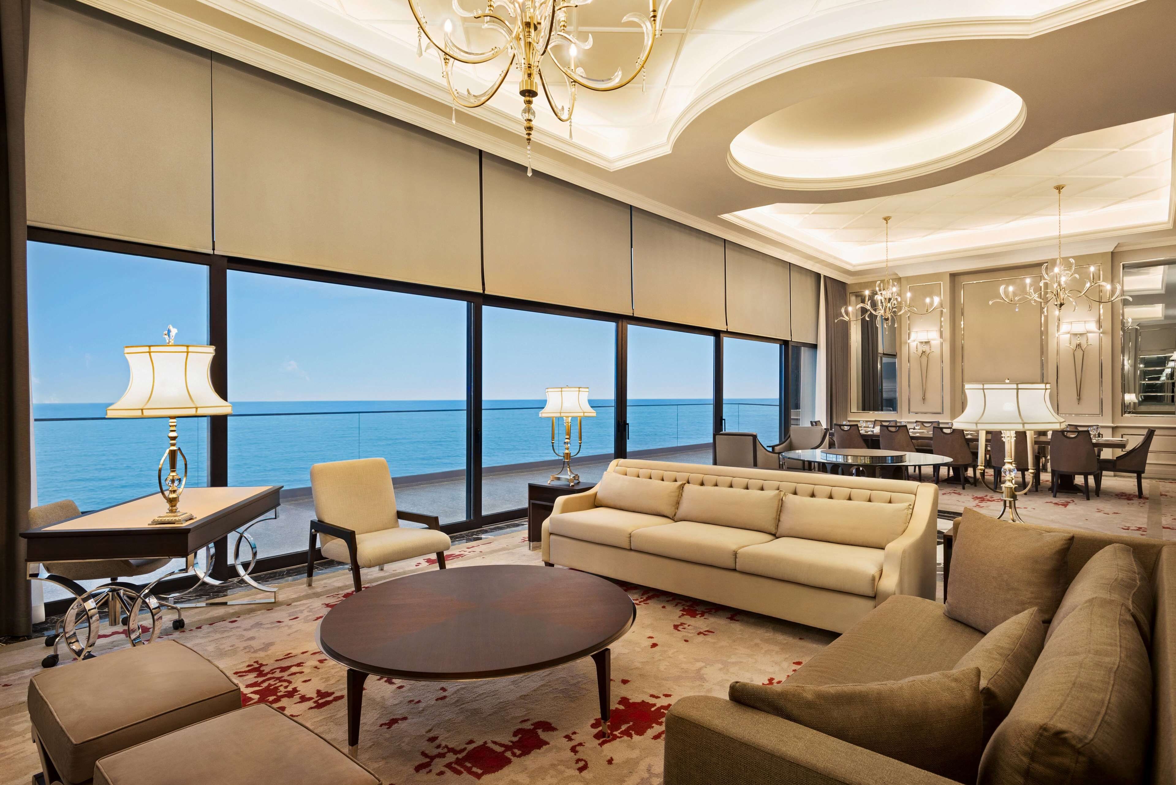 Un vaste espace de vie comprenant une grande fenêtre donnant sur la mer, un canapé, une table basse et un coin repas avec des chaises et une table.
