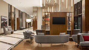 A modern lobby with a sofa, armchairs, a TV, and a wooden bookshelf. - Ramada by Wyndham Rize Findikli (Findikli)