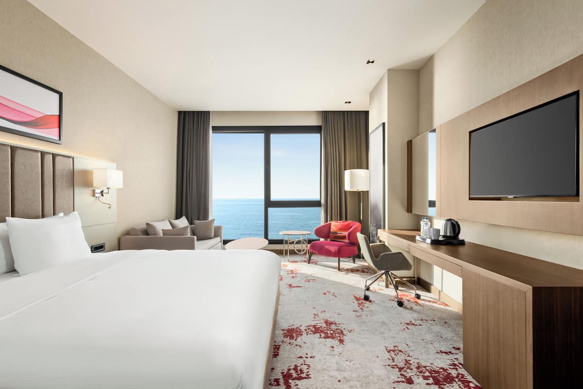 Ein Hotelzimmer mit einem großen Bett, einem Schreibtisch, einem Sessel, einer Couch und einem Fernseher.