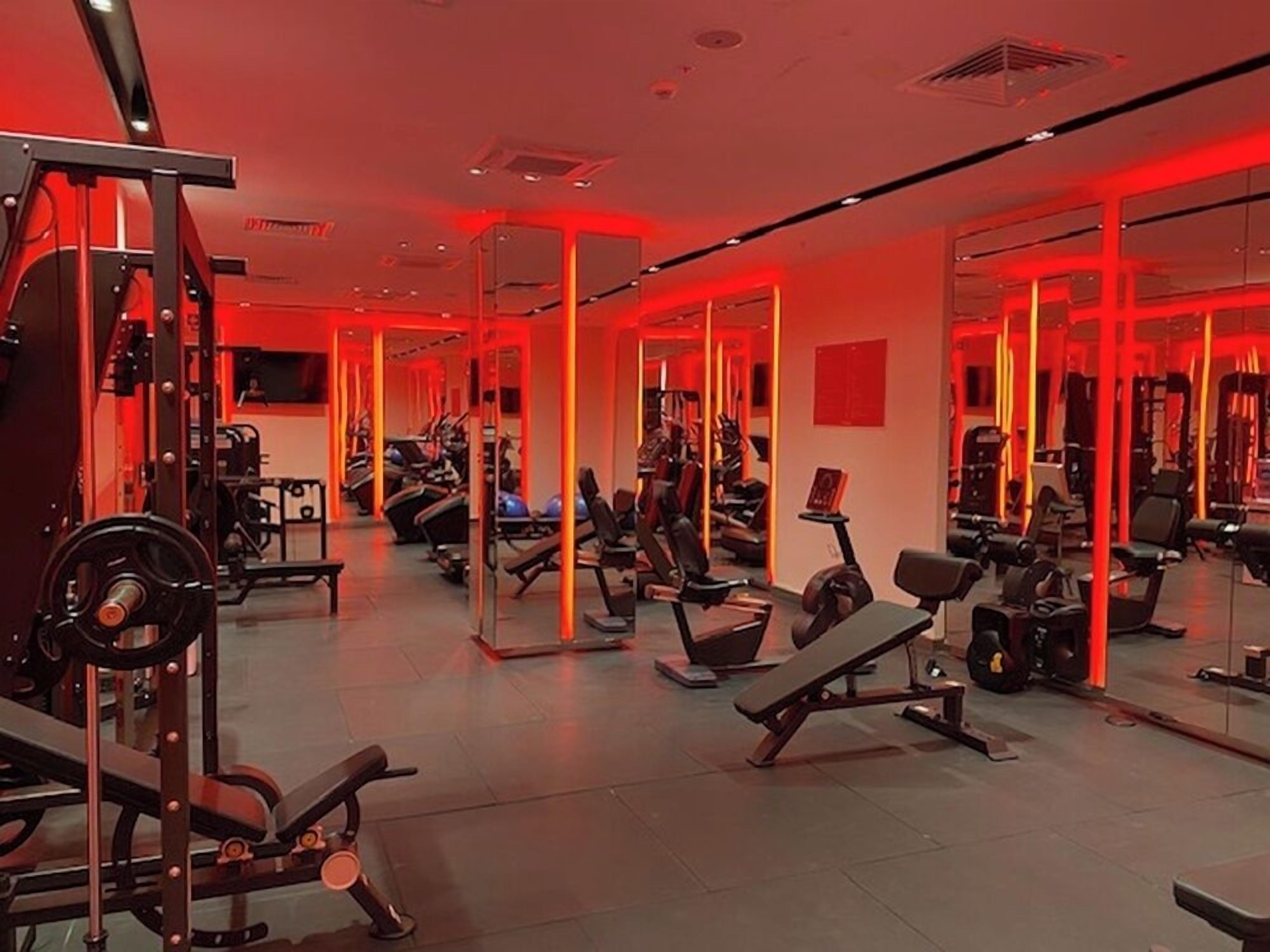 Une salle de sport avec des murs recouverts de miroirs et divers appareils d’exercice.