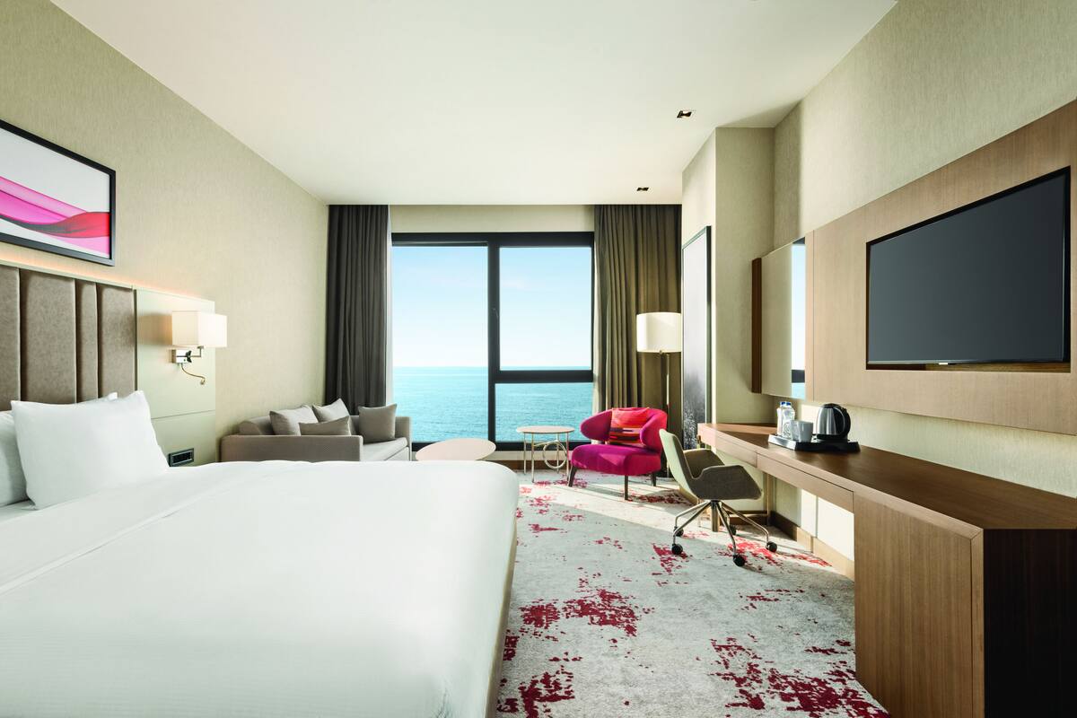 Ein Hotelzimmer mit einem großen Bett, einem Schreibtisch mit Stuhl, einem kleinen Tisch, einer Couch und einem Fernseher.
