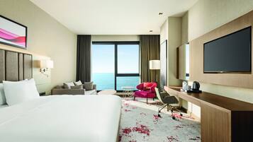 A hotel room with a large bed, a desk with a chair, a small table, a sofa, and a TV.