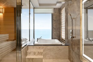 A modern bathroom with a large bathtub, a walk-in shower, and a view of the ocean.