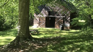 En rustik trælade med en overdækket veranda, omgivet af frodig vegetation og et picnicbord.