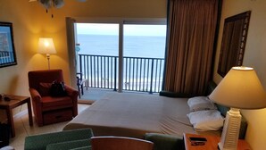 Ein Hotelzimmer mit Bett, Stuhl, Tisch, Lampe und Meerblick vom Balkon.