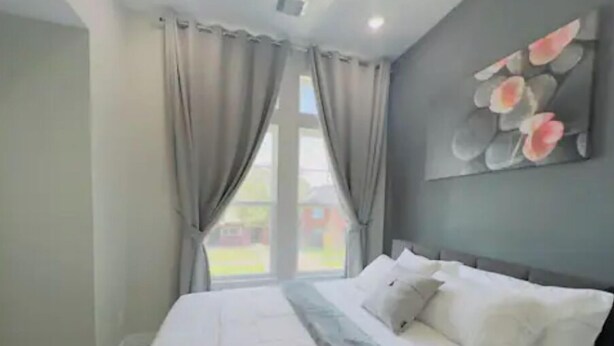 A bedroom with a large bed, beige curtains, and a window with a view of a house. - Gray Lux Hse 3BR|3.5Bath~Downtown|MedCenter|HotTub (Houston)