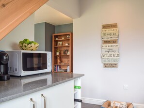 A kitchen with a microwave, a coffee maker, and a wooden shelf with books and decorative items.