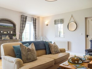 A cozy living room with a sofa, a radiator, a window with curtains, and a wall-mounted mirror. - 1 bedroom accommodation in Richards Castle, near Ludlow (Richards Castle, near Ludlow)