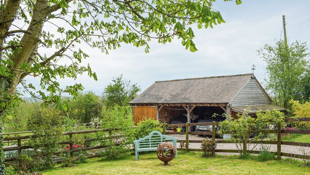 A rural property with a barn, a fenced garden, and a bench.