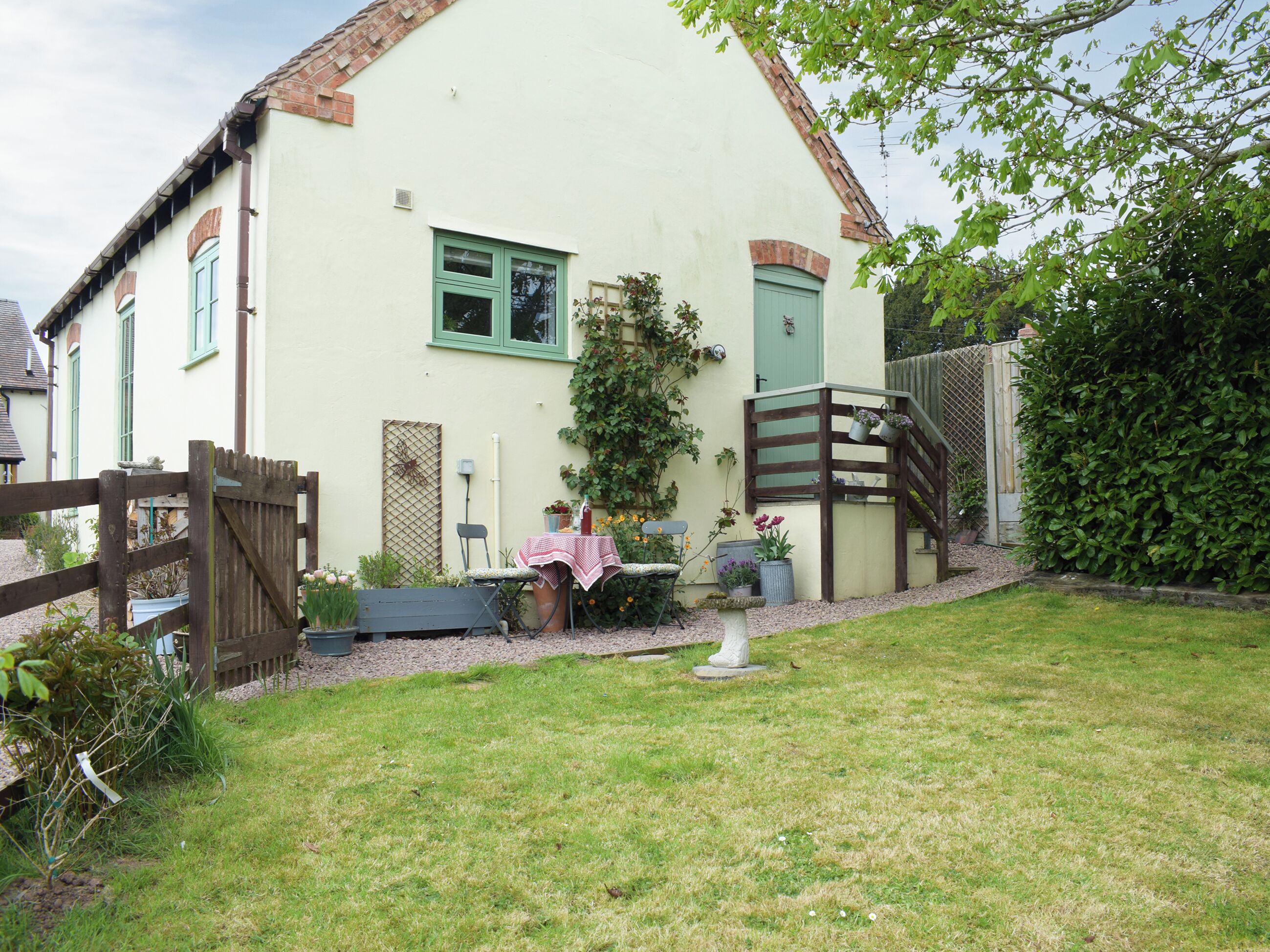 A house with a fenced yard, a wooden staircase, and a table with chairs outside.