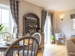 A dining area with a table set for two, chairs, a bookshelf, and a window with curtains. - 1 bedroom accommodation in Richards Castle, near Ludlow (Richards Castle, near Ludlow)