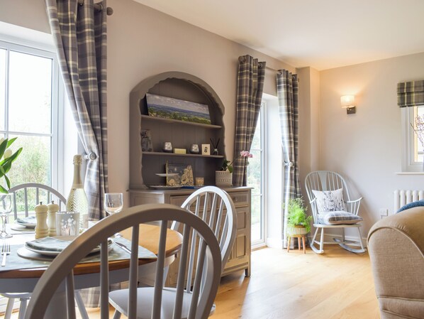 A dining area with a table set for two, chairs, a bookshelf, and a window with curtains. - 1 bedroom accommodation in Richards Castle, near Ludlow (Richards Castle, near Ludlow)