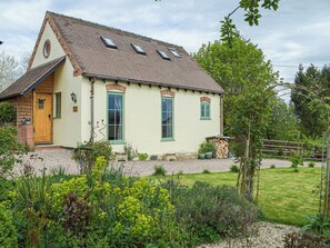 A house with a sloped roof, a front door, and a garden with various plants. - 1 bedroom accommodation in Richards Castle, near Ludlow (Richards Castle, near Ludlow)