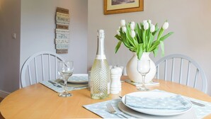 A dining table set with plates, cutlery, glasses, a bottle, and a vase with flowers.