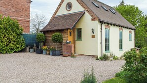 A cottage with a pitched roof, a small porch with potted plants, and a gravel driveway.