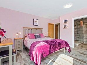 A bedroom with a bed, bedside tables, a desk, and a shower.