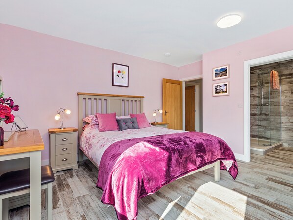 A bedroom with a bed, bedside tables, a desk, and a shower.