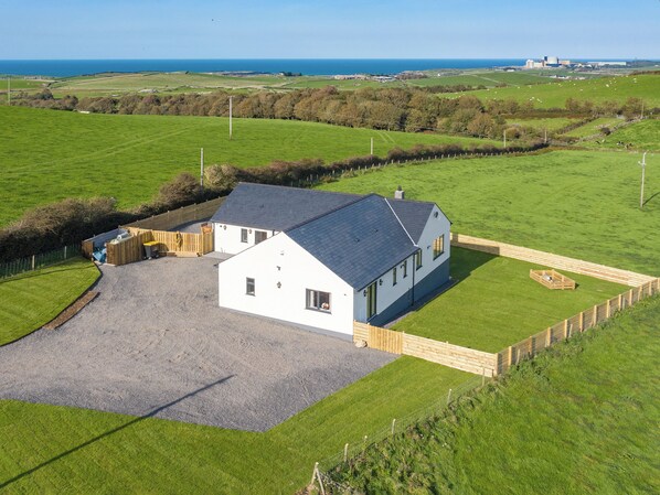 A white house with a grey roof, surrounded by green fields and a body of water in the background.