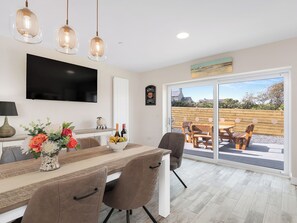 A modern kitchen with a dining area, a TV, and a large sliding glass door leading to an outdoor patio.