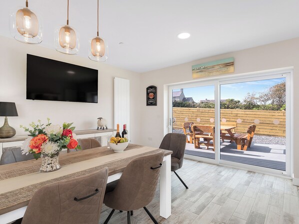 Una cocina moderna con comedor, televisor y un amplio ventanal corredera que da a un patio exterior.