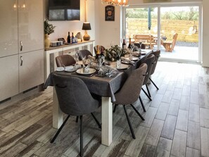 A dining area with a table set for six, a television on the wall, and a wooden deck outside.