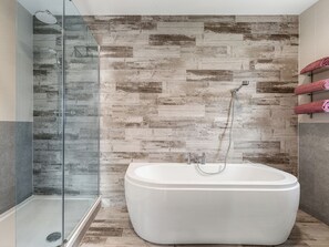 A modern bathroom with a glass-enclosed shower, a freestanding bathtub, and a wooden wall backsplash.