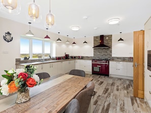 A modern kitchen with a wooden dining table, pendant lights, and a view through the window.