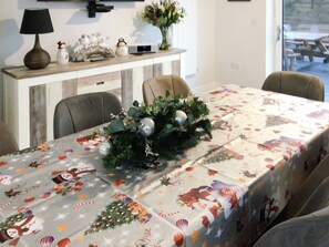 A dining table with a festive tablecloth, chairs, a decorative centerpiece, and a sideboard with various items.