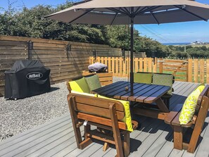 An outdoor patio with a wooden table and chairs, a barbecue grill, and a large umbrella.