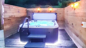 A hot tub in a wooden cabin with a wooden deck and a small step leading up to it.