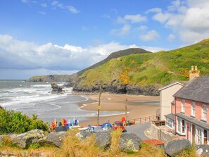 A coastal road with a beach, rocky cliffs, and a building with a red roof.