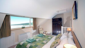Een slaapkamer met een groot raam, een bed met een groen geruit beddegoed, een stoel en een houten garderobe.