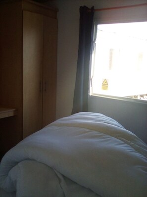 A bedroom with a bed, a wardrobe, and a window with curtains. - River Views Dog Friendly Caravan 3 Bedrooms (Rye)