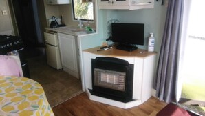 A compact kitchenette with a stove, sink, and a small refrigerator. There is a bed with a patterned bedspread and a window with curtains. - River Views Dog Friendly Caravan 3 Bedrooms (Rye)