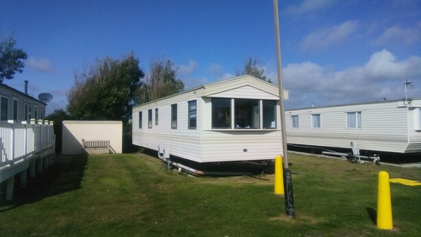 A mobile home with a front porch and a small deck, surrounded by other mobile homes and a grassy area. - River Views Dog Friendly Caravan 3 Bedrooms (Rye)