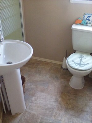 A bathroom with a white sink, a toilet with an anchor design, and a window with a view of the outside. - River Views Dog Friendly Caravan 3 Bedrooms (Rye)