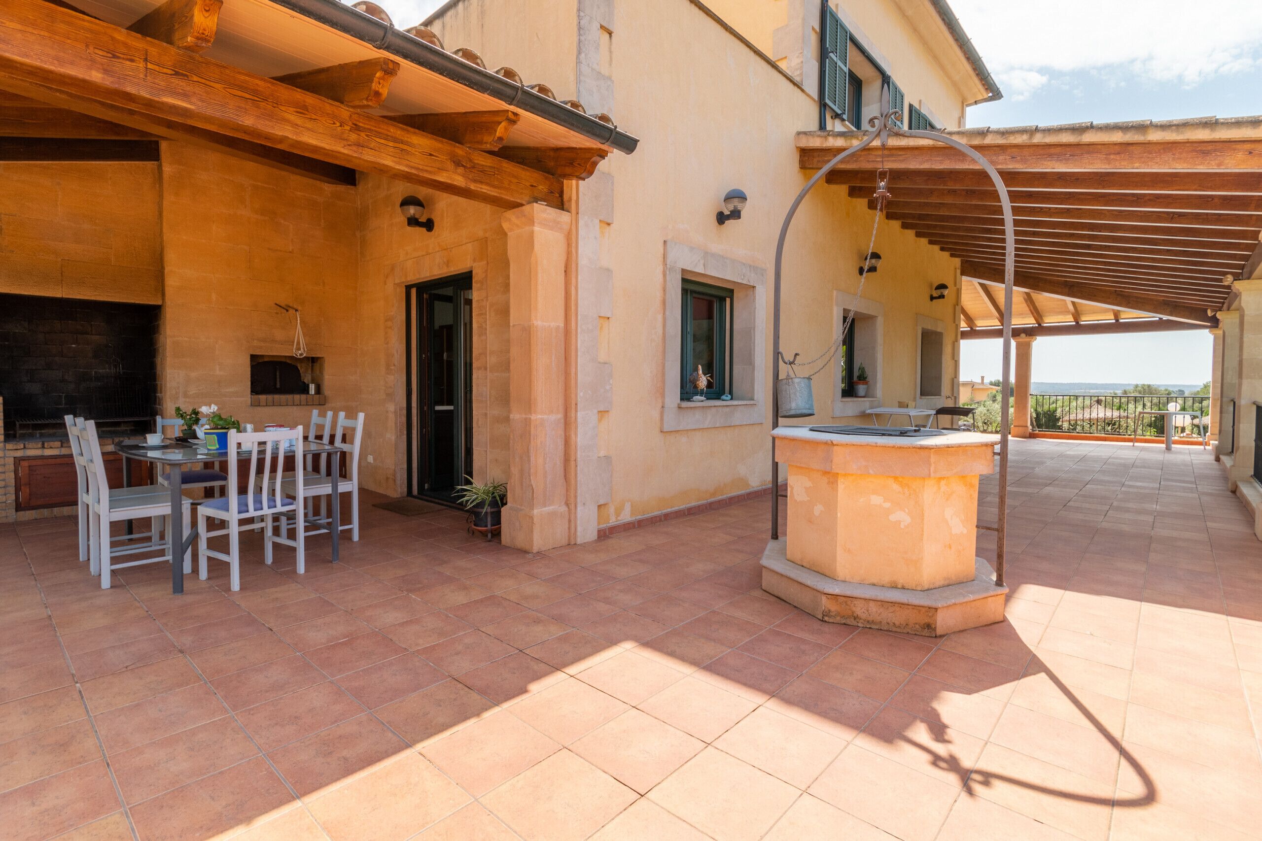 Un espace patio aménagé avec une table et des chaises, une cheminée en pierre et une pergola agrémentée d’un luminaire suspendu.