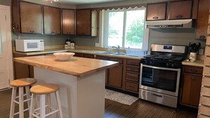 A kitchen with wooden cabinets, a central island with stools, a microwave, a stove, and a sink.