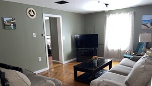 A living room with two grey sofas, a black coffee table, a flat-screen TV, and a window with curtains.