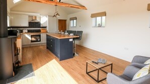 A spacious kitchen with wooden beams, a central island, and a dining area with a sofa and coffee table. - Glowty Brynbedw (Clynderwen)
