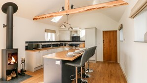 A modern kitchen with a central island, a built-in wood stove, and a dining area with bar stools. - Glowty Brynbedw (Clynderwen)