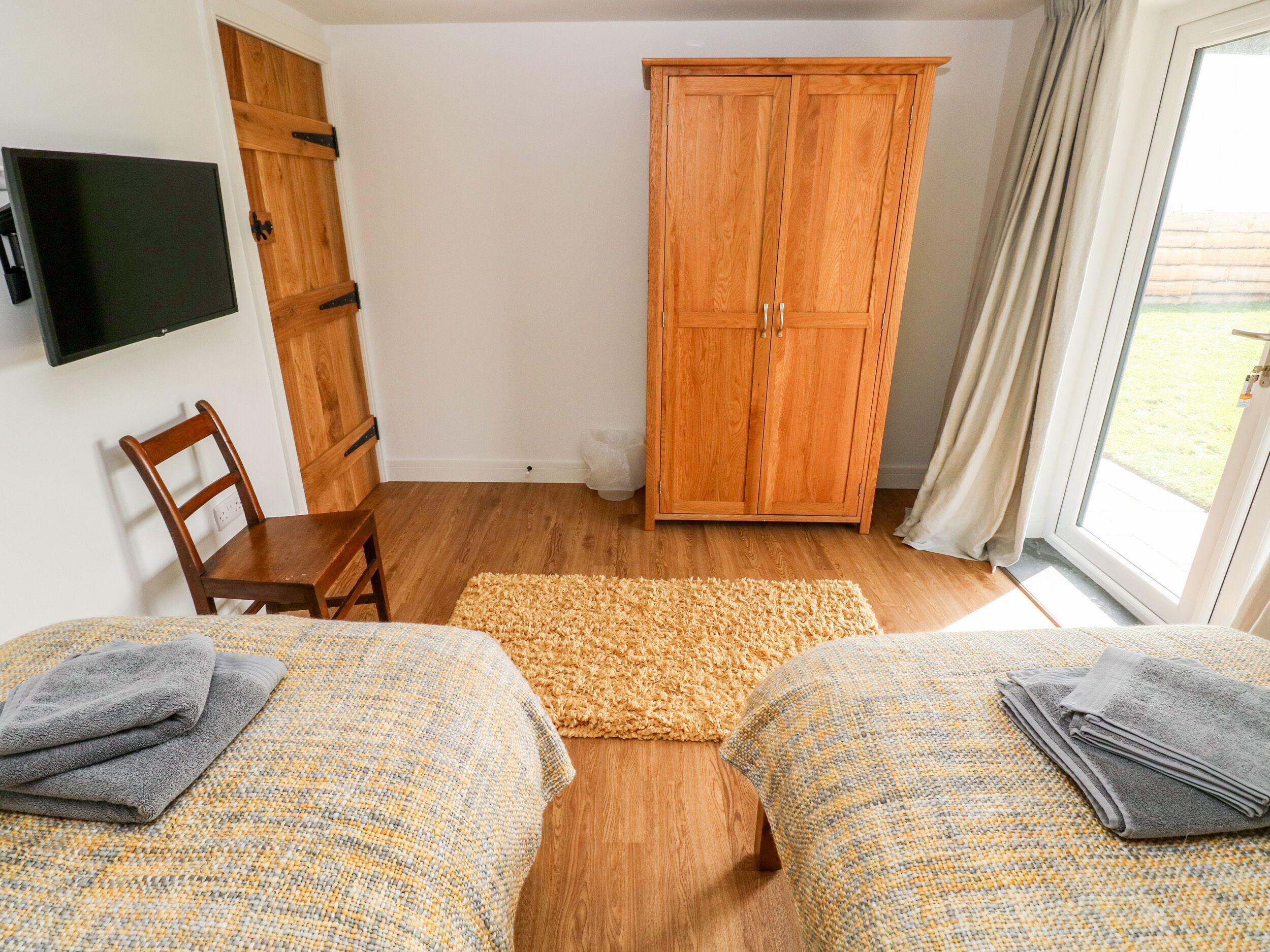 Une chambre avec deux lits, une armoire en bois, une télévision et une fenêtre avec des rideaux.
