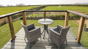 A deck with two wicker chairs and a round table, overlooking a grassy field with a fence and a soccer goal in the distance. - Glowty Brynbedw (Clynderwen)
