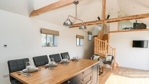 A modern dining area with a wooden table set for six, black upholstered chairs, a built-in black cabinet with drawers, and a wooden staircase leading to an upper level. - Glowty Brynbedw (Clynderwen)