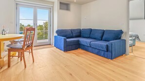 A modern living room with a blue sectional sofa, wooden flooring, a dining table with chairs, and a large sliding glass door leading to an outdoor balcony. - Rogeston House is a stunning and unusual annexe added to the original house. (Johnston, near Haverfordwest)